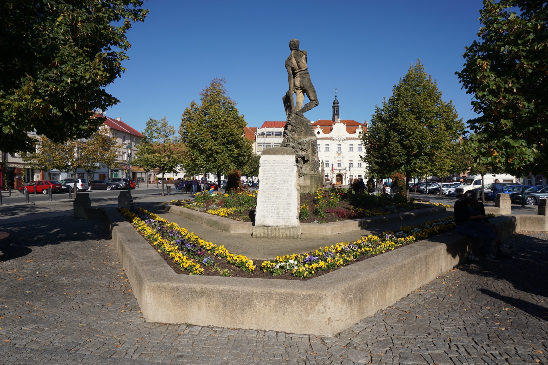 Husovo náměstí v Berouně s kašnou, květinovými záhony a měšťanskými domy