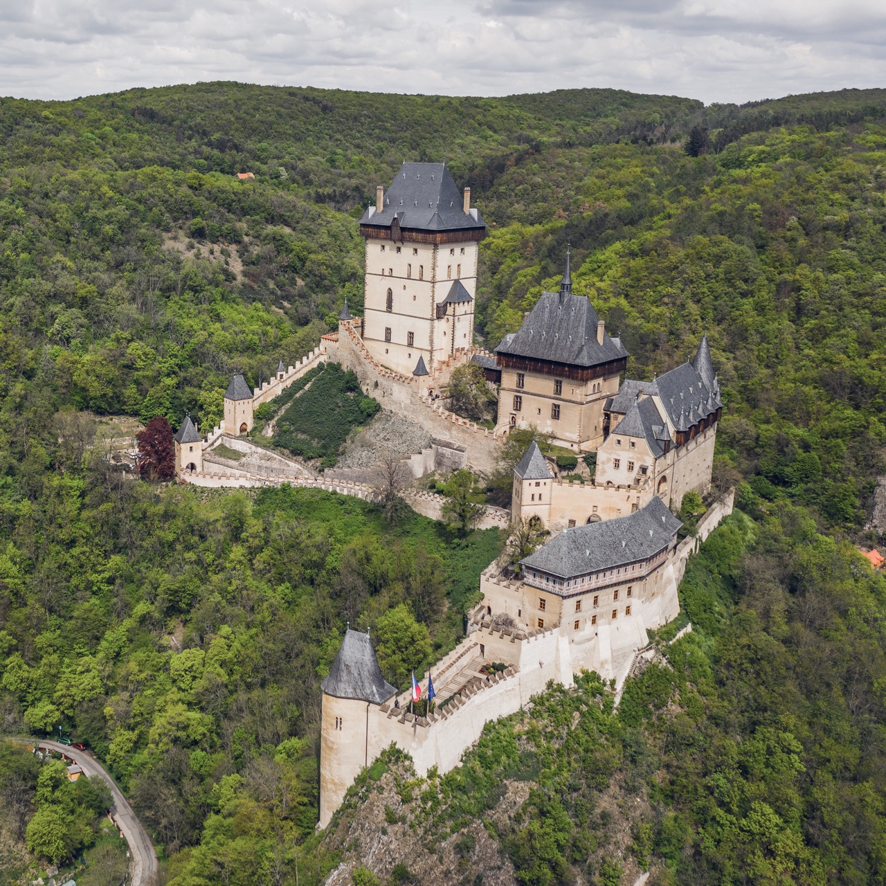 Letecký pohled na hrad Karlštejn s hradbami nad zalesněným údolím